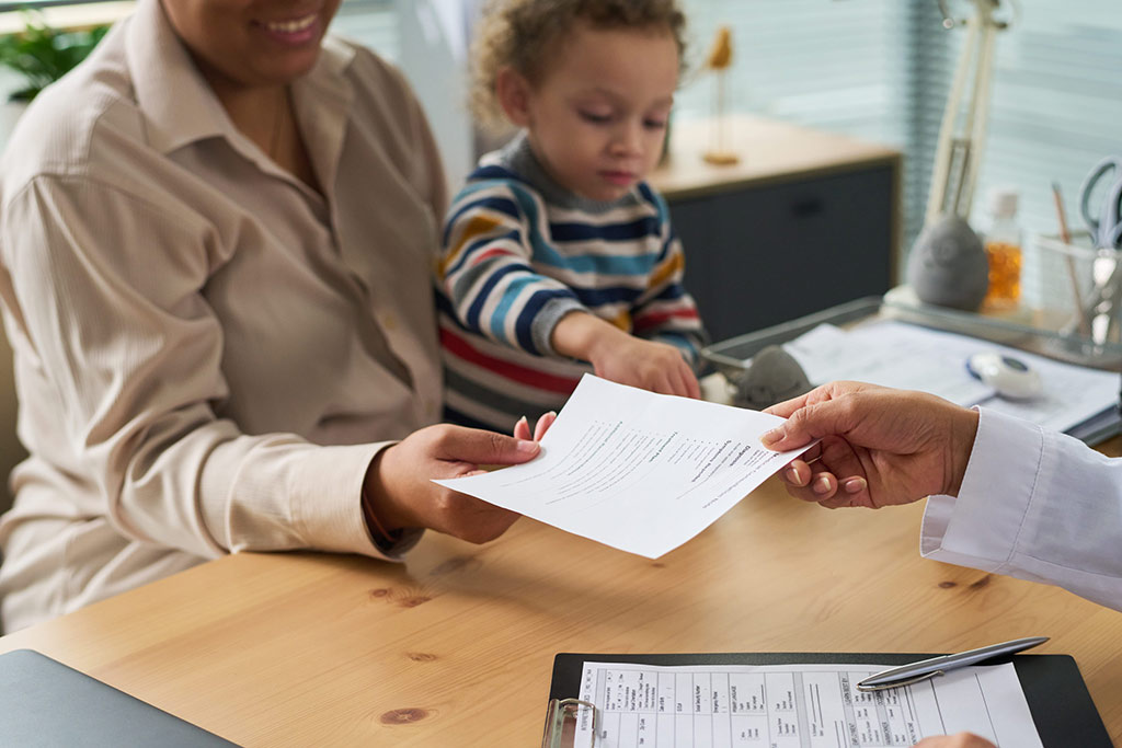 Woman holding a child and receiving a document from another person at a desk